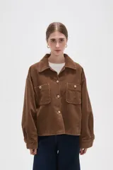 Sobrecamisa de pana color marrón, con cuello camisero, cierre frontal con botones dorados y dos bolsillos frontales con solapa. Presenta mangas largas con puños abotonados y un corte recto y holgado.