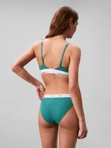 Conjunto de ropa interior de dos piezas compuesto por un corpiño triangular y una bombacha tipo tanga, ambos confeccionados en algodón con textura acanalada en color verde azulado. El corpiño cuenta con tirantes finos ajustables y una banda elástica inferior con el logo de la marca, mientras que la bombacha presenta un corte de talle medio con la misma banda elástica distintiva.