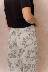 Jean wide leg de tiro alto con estampado floral integral en tonos grises sobre base beige. Cuenta con cierre frontal con botón, pasacintos y bolsillos funcionales delanteros y traseros.