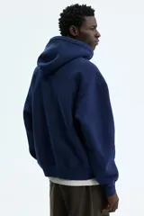 Campera con capucha y cierre frontal de color azul marino, corte oversized, bolsillos tipo canguro y estampado universitario "SOHO NYC ATH DEPT" en el pecho.