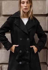 Trench clásico de largo midi en color beige, con diseño de doble abotonadura, solapas amplias, detalles en hombros y correas ajustables en los puños.