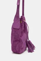 Mini bandolera de piel color morado, de diseño tipo saco con cierre fruncido y cordón ajustable con borlas en el extremo. Cuenta con asa larga ajustable y detalles metálicos dorados.