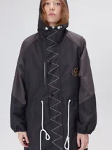 Campera tipo piloto con capucha, cierre frontal con botones y detalle de costuras en zigzag. Presenta cordones ajustables en la cintura y capucha, puños elásticos y logo bordado en el pecho.