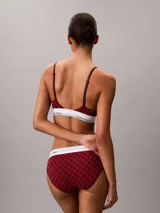 Bralette Calvin Klein de corte triangular, confeccionado en mezcla de algodón elástico y modal, con estampado gráfico en tonos rojos y banda elástica inferior en color blanco con el nombre de la marca en contraste.