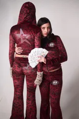 Conjunto de buzo y pantalón de terciopelo rojo con estampado animal print negro. El buzo es de corte ajustado, con capucha y cierre frontal. El pantalón es de corte acampanado y tiene un aplique de estrella de strass en la parte trasera.