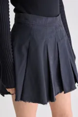 Minifalda plisada de algodón azul oscuro, con silueta evasé, cierre lateral con cremallera y terminación desmechada en el ruedo.