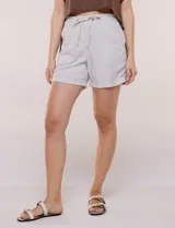 Short de lino de corte recto, color beige, con cintura elastizada y cordón ajustable. Cuenta con bolsillos delanteros aplicados, bolsillos traseros funcionales y ruedo con dobladillo fijo arremangado, detallado en los laterales con presilla y botón a contraste.