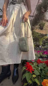 Bandolera compacta color rosado, con correa regulable y desmontable. Tiene apertura superior, bolsillo frontal con cierre y detalle de borla, y bolsillo trasero sin cierre. El interior está forrado en tela y cuenta con un bolsillo adicional.