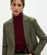 Blazer de sastrería color verde oliva, con corte oversized, solapas clásicas, cierre frontal de un botón y bolsillos con tapa. Cuenta con forro interno y textura sutil.