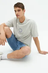 Remera de manga corta color gris claro, con corte regular y estampado circular con texto en relieve en el pecho.