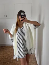 Vestido corto de tejido tipo crochet a rayas horizontales blancas y negras, con escote en V y mangas tres cuartos. El diseño incluye flecos en el ruedo y se complementa con un kimono tejido de color blanco.