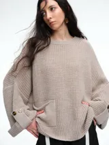 Sweater de tejido tipo waffle color beige, con corte amplio y relajado. Presenta cuello redondo, hombros caídos, un bolsillo frontal aplicado y puños anchos decorados con botones.