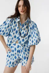 Short de lino blanco con estampado floral azul, de tiro alto, con bolsillos laterales y cierre frontal con gancho metálico.