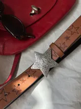 Cinturón marrón de cuero sintético con estrellas grabadas y hebilla plateada en forma de estrella.