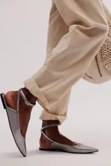 Zapato plano negro de cuero, tipo chatita, con punta fina y tiras con hebilla ajustable alrededor del tobillo.