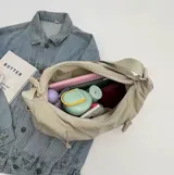 Bolso hobo grande color gris topo, de tela suave y liviana, con correa de hombro ajustable y dos bolsillos frontales con cierre.