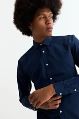 Camisa de manga larga en color beige, confeccionada en algodón, con cuello clásico y cierre frontal de botones.