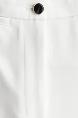 Pantalón sastrero de color blanco, tiro alto, con cierre frontal de botón y piernas acampanadas con pliegues marcados.