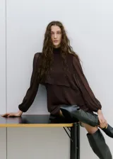 Vestido corto marrón con estampado de lunares, cuello alto y diseño de capas superpuestas con volados. Mangas largas abullonadas semitransparentes.