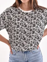 Remera de manga corta color beige con estampado de bananas en tonos amarillo, naranja y rosado.