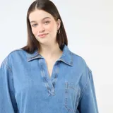 Blusa recta de jean azul claro, con cuello camisero, escote en V con abertura y un bolsillo aplicado en el pecho.