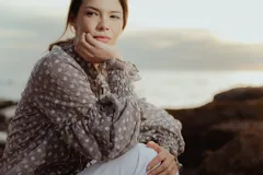 Blusa color gris con estampado floral blanco, cuello mao con lazo, mangas largas abullonadas con puños elásticos.