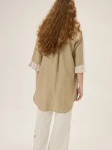 Camisa de lino de silueta relajada y largo irregular, color beige, con cuello mao, botones frontales a contratono y mangas tres cuartos terminadas en volados.