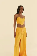 Pantalón amarillo de lino y viscosa, de pierna ancha, con cintura alta, pretina recta en la parte delantera y elástica en la parte trasera. Presenta detalle de trenza vertical en los laterales y aberturas en el dobladillo.