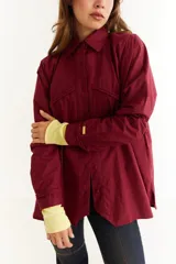 Camisa de corte oversize color bordó, con cuello clásico, cierre frontal de botones y detalle de trenzado horizontal en la parte superior delantera. Posee mangas largas con puños abotonados.