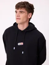 Canguro marrón con capucha y bolsillo frontal, con un diseño gráfico colorido en la espalda que representa una casa surrealista con el texto 'Supreal State of Mind'.