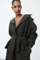 Trench corto de corte fluido confeccionado en mezcla de lyocell, color verde militar. Presenta cuello solapa, cierre frontal cruzado con botón, mangas largas con hombro caído y puños con trabilla. Incluye bolsillos delanteros de plastrón y cinturón de lazada en el mismo tejido.
