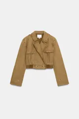 Trench corto de cuello solapa y manga larga, con diseño cruzado y cierre frontal con botones. Presenta bajo acabado en elástico y trabillas en los hombros.