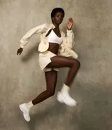 Short deportivo color beige, modelo runner, confeccionado en poliamida, con cintura elástica y lazo. Presenta recortes con hilo reflectante y un bajo redondeado.