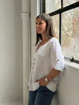 Blusa blanca de lino, con escote en V y tres botones frontales grandes de madera. Cuenta con mangas tres cuartos con presilla y botón para arremangar.