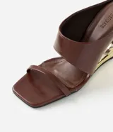 Sandalias tipo mule de color marrón, con tiras anchas en el empeine, tira fina separadora de dedos, puntera cuadrada y taco chino calado con acabado dorado metalizado.
