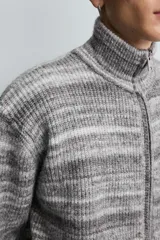 Chaqueta de punto con diseño de rayas horizontales en tonos grises, cuello subido y cierre frontal de cremallera completa. Presenta un corte relajado y acabados en rib en puños y bajo.