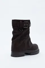 Bota de caña media color negro, con suela robusta dentada y detalle de hebilla ajustable en la parte superior. Presenta una argolla metálica lateral y un diseño de estética urbana con acabado texturizado.