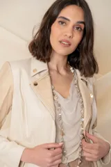 Chaqueta corta cruzada de cuero vegano color marfil, combinada con tela rayada color oro, con cierres metálicos y tachas doradas.