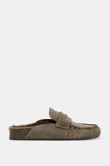 Zueco destalonado tipo mocasín confeccionado en piel, con interior forrado en pelo sintético. Presenta antifaz en el empeine, costuras decorativas y punta redonda.