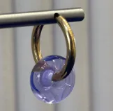 Aros tipo argolla de oro con dije colgante en forma de dona de vidrio color lila.