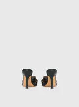 Mules de cuero negro con punta fina, diseño abierto en los laterales y tiras decorativas con ojales metálicos y hebilla ajustable.