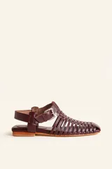 Sandalias planas de cuero color marrón oscuro, estilo huarache con tiras entrelazadas, puntera cuadrada y tira ajustable con hebilla en el talón.