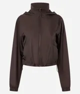 Campera cortavientos de corte cropped, color marrón oscuro, con capucha estructurada, cierre frontal por cremallera, bajo ajustable con cordón y puños elásticos.
