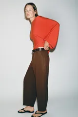 Pantalón tiro bajo color marrón, de corte globo y pernera recta con raya marcada al frente. Incluye trabillas y un cinturón marrón oscuro con hebilla metálica.