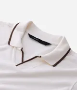 Camisa polo de manga corta confeccionada en algodón, con cuello en V y detalles en color contrastante en el cuello y los puños. Presenta un diseño de tejido en media malla, ofreciendo una textura suave y transpirable.