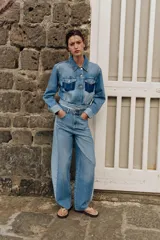 Jeans de tiro medio con diseño barrel y paneles laterales en un tono de denim más claro que contrasta con el centro. Presenta cinco bolsillos, cierre frontal con cremallera y botón, y bajo con acabado sin costura.