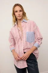Camisa de corte oversized confeccionada en broderie de algodón con diseño combinado. Presenta un estampado de rayas verticales en tonos rojos y blancos, con detalles en contraste de color azul en el cuello, los puños y el bolsillo frontal. Posee cierre frontal con botones y mangas largas.