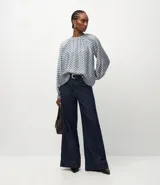 Blusa de mangas largas abullonadas con cuello redondo fruncido y diseño de estampa geométrica en tonos azul y blanco.