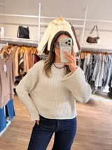 Sweater de punto canalé en color beige, con diseño de cuello bote, mangas largas amplias y corte crop. Presenta una textura acanalada vertical que recorre toda la prenda.