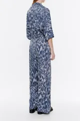 Mono largo de viscosa con estampado abstracto en tonos azules y grises. Tiene cuello camisero con solapa, manga corta murciélago con fruncidos en los hombros, cierre frontal con cremallera oculta, bolsillos con tapeta redondeada en el pecho y con fuelle en la cadera, y cinturón de tela.